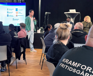 Man med mikrofon talar till konferensdeltagare.